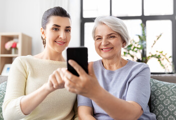 family, generation and technology concept - happy smiling senior mother and adult daughter with smartphone at home