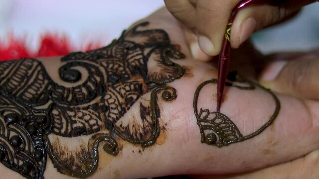 Woman designing Henna or Mehendi Tatto on the palm of a girl. Handheld closeup