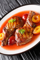 grilled pork chop with ripe plums and sauce close-up in a plate on the table. vertical