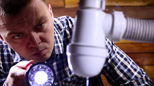 Man plumber with flashlight discovered a water leak problem in the kitchen or bathroom