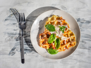 Zucchini waffles with sauce and basil leaves and sauce on a light gray plate