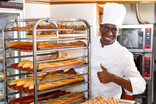 Cheerful baker in white uniform giving thumbs up, satisfied with fresh baked products in his bakery - Powered by Adobe