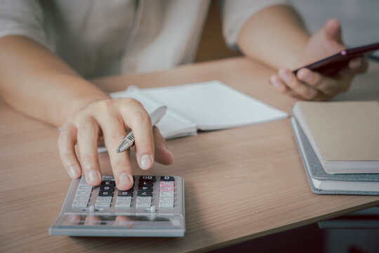 Business & Finance concept. Close up hand of young Asian man wear white shirt ongoing to calculate home loan mortgage to summary expense payment or accounting with using smartphone on office deck