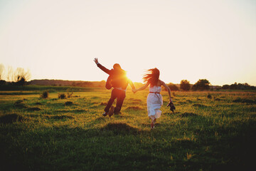 Lovely young couple are having fun and running outdoors in the field on summer day. romantic photo at sunset time. love story.