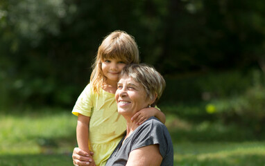 Fototapeta premium Child girl embracing Grandmother spending time together in nature. Concept of friendly family. Quality Time. copy space 