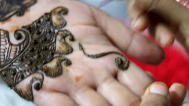 Closeup of Woman designing Henna or Mehendi Tatto on the palm of a girl.