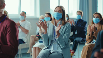 Corporate diverse business people clapping hands at successful conference. Group of happy business people in face masks sitting together on meeting seminar. Quarantine. Workspace.