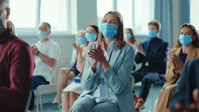 Corporate diverse business people clapping hands at successful conference. Group of happy business people in face masks sitting together on meeting seminar. Quarantine. Workspace.
