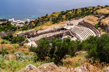 MILOS, Greece. Ruins of Ancient Theater of Milos on a green hill with Mediterranean Sea in the...