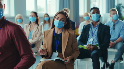 Female journalist in medical mask asking the speaker on business seminar. Diverse corporate people...