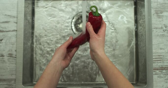 Female hands wash red Ramiro pepper by stream of water. Close up top shot