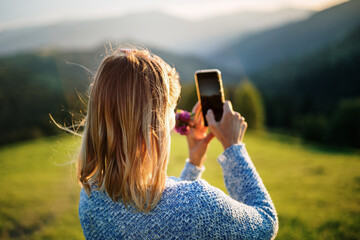 Young woman traveler take photo of beautiful sundown in mounting with mobile phone camera. Focused on sun glare girl's hair