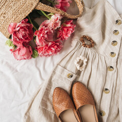 Beauty fashion collage with women's clothes and accessory on white linen. Sun dress sarafan, leather shoes, pink peony flowers in straw bag. Flat lay, top view fashion blog lifestyle concept