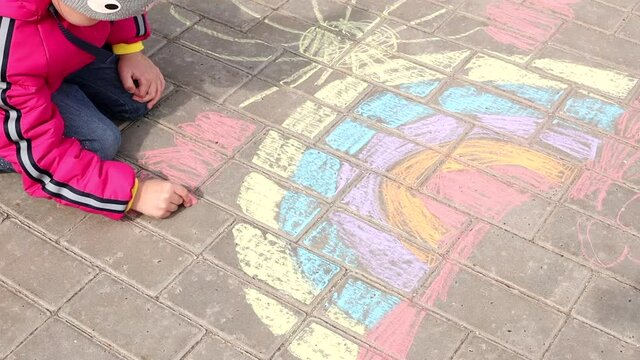 A child draws a rainbow and sun on the asphalt. A little girl draws chalk in the park.
