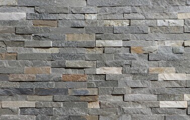 Stone wall cladding made of horizontal gray, brown and white strips of rock stacked . Background...