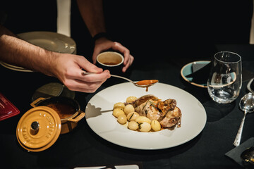 Manos sirviendo salsa sobre plato de pollo guisado con &ntilde;oquis