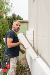 Repairman applying styrofoam board with applied cement glue onto house exterior