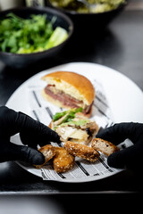 Manos de chef colocando trozos de pollo rebozado en plato con hamburguesa de fondo