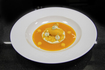 High cuisine dessert: Mango Ice cream  with jelly mango fruit in a white meringue, on a black background. 45 degree view angle on a isolated ceramic white plate. 