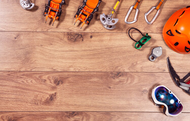 Climbing adventure equipment flat lay view. Top view of extreme mounteneering tools like helmet, campons, ice axe, carabiner, glasses. Copy space on wood.