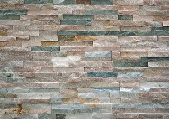 Stone cladding wall made of  striped stacked slabs of natural rocks. Colors are various, from dark green to white. Panel for exterior.