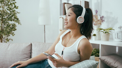 holiday pastime chinese lady wearing headset is listening favorite pop music at home. pleasant...