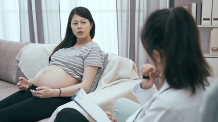 depressed asian pregnant woman visiting psychologist doctor in clinic at reception. young future...