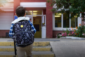 Child boy with bag go to elementary school. Back view