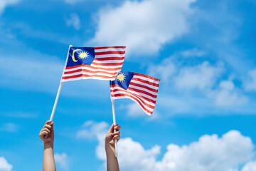 Hand happily waving Malaysia flag against blue sky.