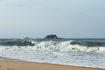 The huge waves crashing into ston island against the blue sky and horizon at summer sea shore.