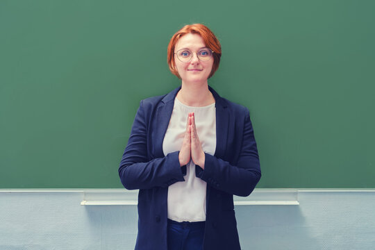 Woman teacher stands at the school blackboard clasped hands in prayer, copy space