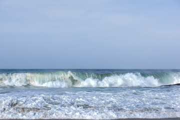 The huge waves crashing into ston island against the blue sky and horizon at summer sea shore.