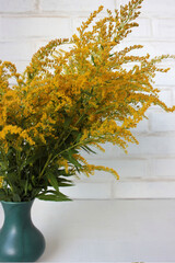 Fototapeta na wymiar Bouquet of yellow flowers in vase on the white brick wall background. Autumn still life
