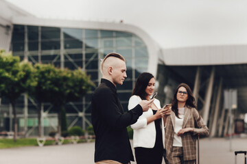 Friends waiting for the flight, standing near the airport, using mobile phones