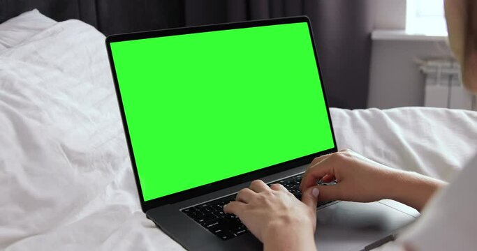 Young girl searching internet sitting in modern hotel room. Tourist resting after eventful day. Close-up of female hands typing on computer. Green screen monitor