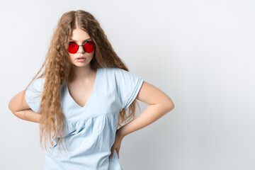 Portrait of charismatic modern girl with curly long hair in casual light clothes and wears round red spectacles posing isolated on white wall background. People lifestyle concept