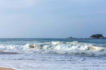 The huge waves crashing into ston island against the blue sky and horizon at summer sea shore.