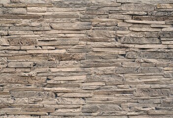 Stone cladding wall made of  striped stacked thin slabs of natural brown rocks stained with black .