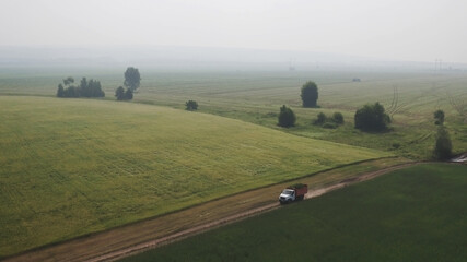 Aerial view truck carries freshly cut feed crop to farm on country road across field. Farmers will use plants for animal feed, preparing feed for winter. Modern Technologies in Agriculture