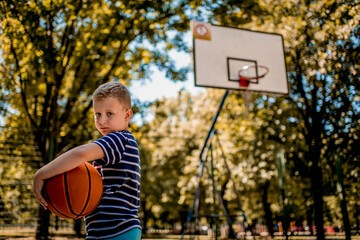 Boy holding a basketball ball at the outdoor courtyard.