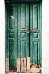Close-up of shabby green wooden doors locked with a broken bottom and planks at the entrance.