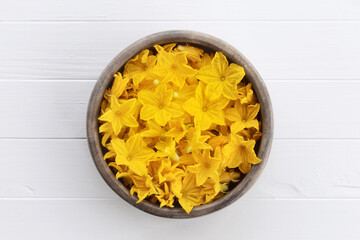 Cucumber flowers in a wooden bowl. Edible cucumber flowers  on a white wooden table.  Cuisine ingredient. Concept of edible flowers.