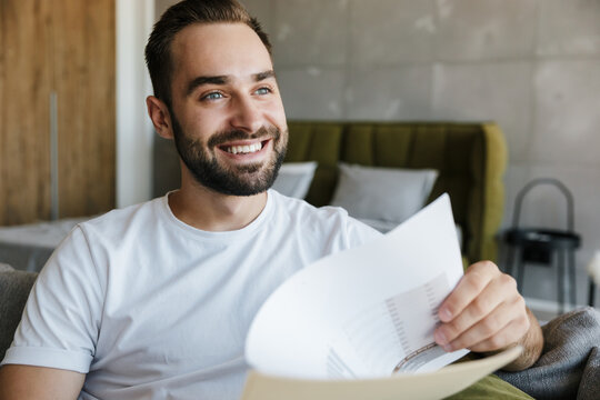Image of young joyful man working with papers while sitting on couch