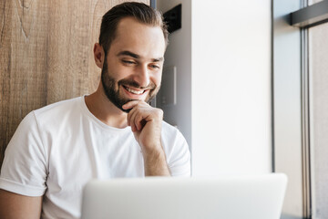 Image of young cheerful man using laptop and smiling