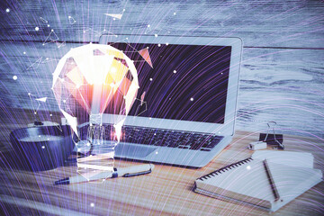 Computer on desktop in office with bulb icon hologram. Double exposure. Concept of idea.