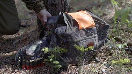 Man lifts backpack over strap from ground in forest. Man in camouflage clothes hunts outdoor in forest hunting alone. Hiker walking in forest.