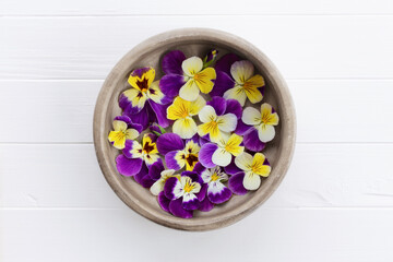 Obraz na płótnie Canvas Pansies in a wooden bowl. Edible flowers, field pansies, violets on a white wooden table. Concept of edible flowers. Cuisine ingredient, condiment.