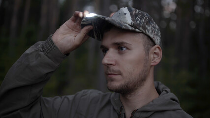 Portrait of handsome young man hunter or tourist. Man puts on his head cap with diode flashlight on...