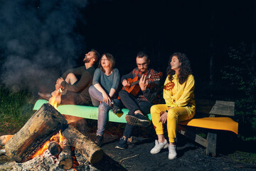 Fototapeta na wymiar Friends playing guitar near bonfire in night forest.