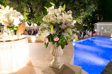 in the evening in a very interesting place a beautiful bouquet of white roses a swimming pool with blue waters illuminated for an unforgettable wedding ceremony between an Italian man and woman